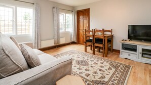 A living room with a sofa, a dining table with chairs, a TV, and a large window with curtains. - Wisteria Chalet (Highbridge)