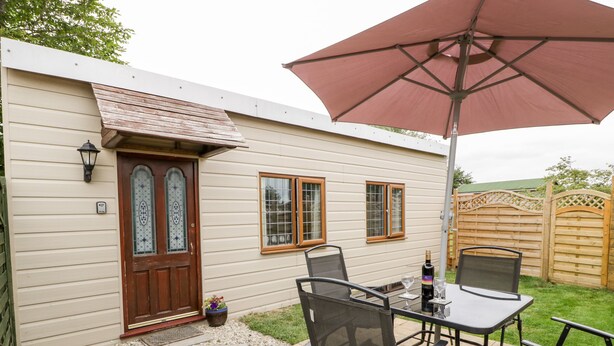 A patio with a table and chairs, a wooden door, and a large umbrella. - Wisteria Chalet (Highbridge)