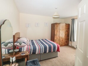 A bedroom with a bed, a wardrobe, a mirror, and a small table. - Dunholme House (Teignmouth)