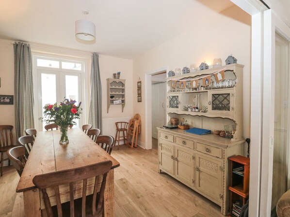 A dining area with a wooden table and chairs, a vase of flowers, and a vintage cabinet with glassware and decorations. - Dunholme House (Teignmouth)