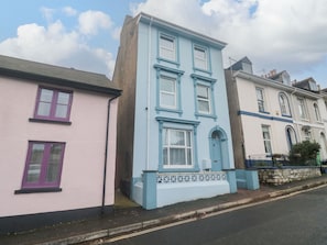 A row of colorful houses with distinct architectural styles, including a pink house with purple shutters, a blue house with white trim, and a cream-colored house with blue accents. - Dunholme House (Teignmouth)