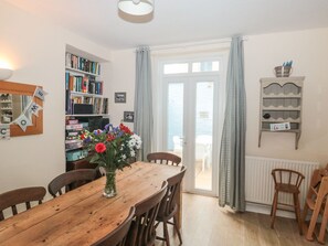 A dining area with a wooden table and chairs, a bookshelf, a welcome sign, and a view through a glass door. - Dunholme House (Teignmouth)