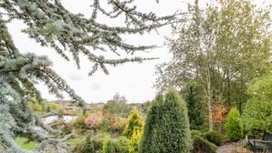 A garden with various trees and shrubs, a wooden path, and a river in the background. - The Stilehouse Apartment (Worcester)