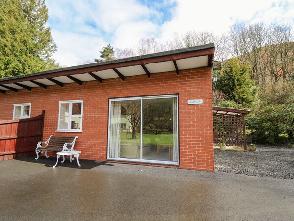 Ein Backsteinhaus mit überdachter Terrasse, einer Schiebetür und einer hölzernen Bank.