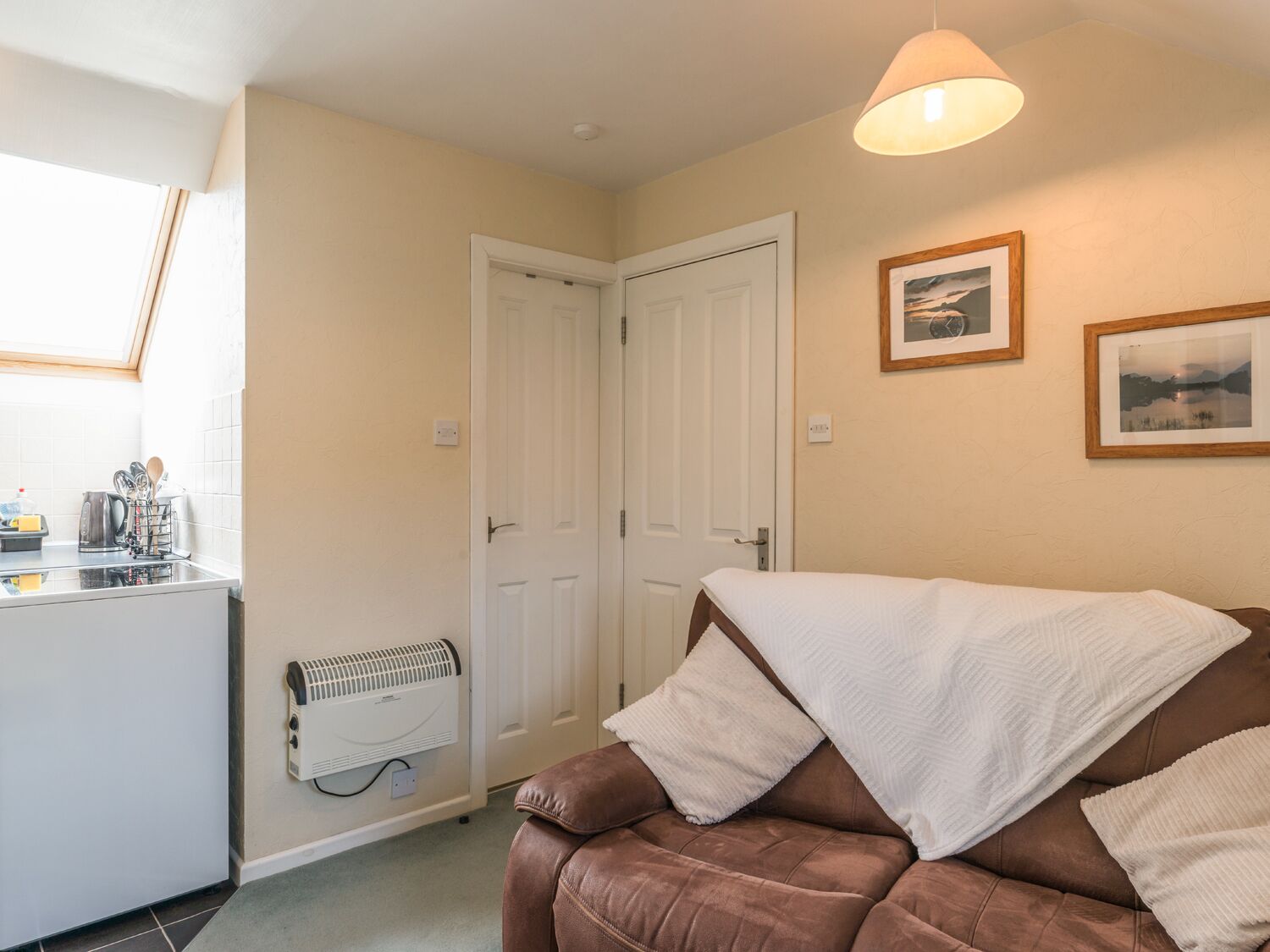 A cozy room with a brown leather sofa, a white radiator, and a small kitchen area with a kettle and utensils.
