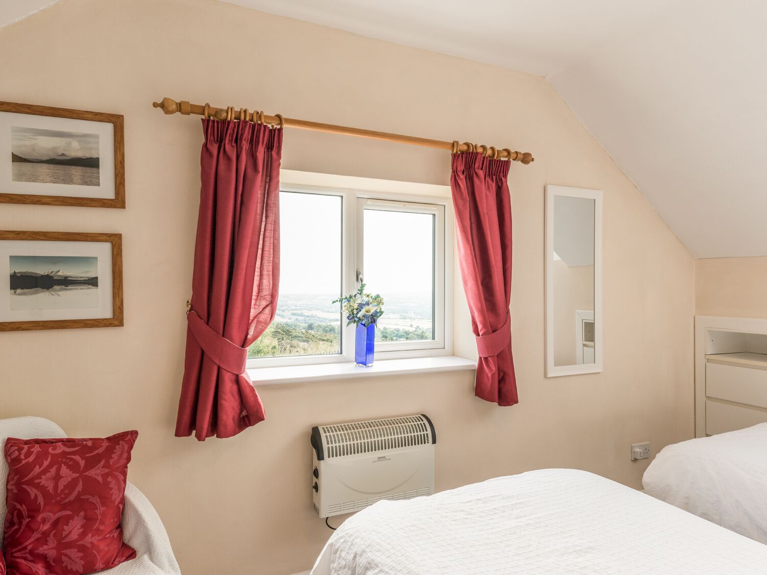 A bedroom with a bed, a radiator, a window with curtains, and framed pictures on the wall.