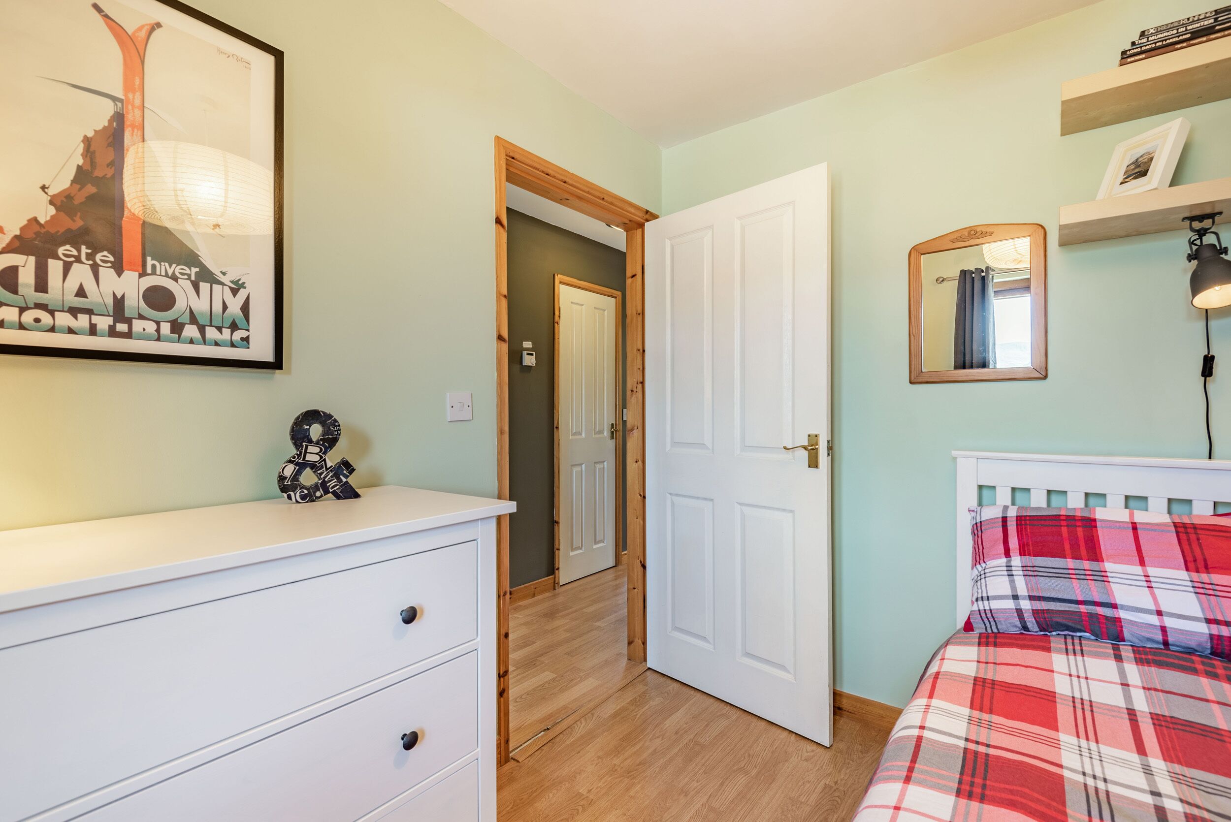 A bedroom with a bed, a dresser, a door, and a wall with a framed picture.
