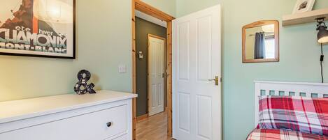 A bedroom with a bed, a dresser, a door, and a wall with a framed picture.