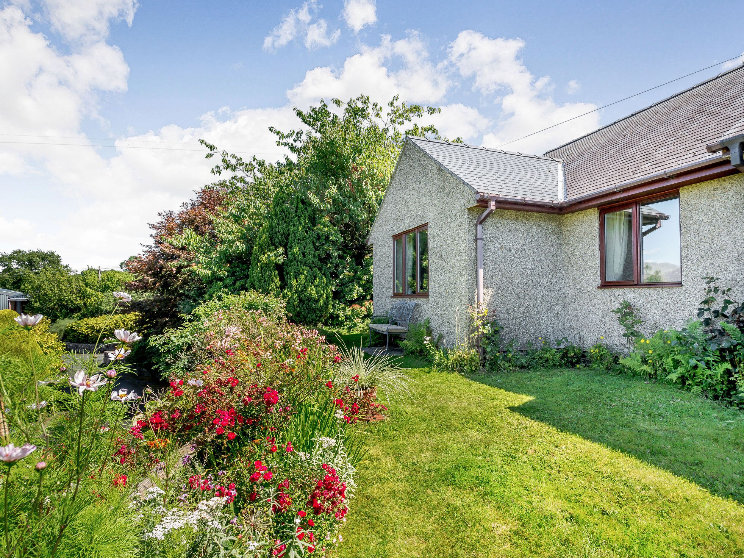 A house with a sloped roof, a small porch, and a well-maintained garden with various flowers and shrubs.