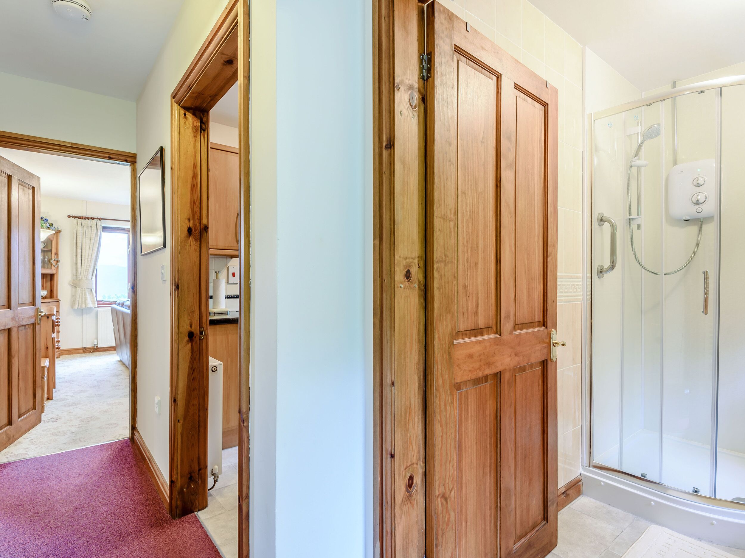 A hallway with wooden doors leading to a bathroom with a glass shower enclosure.