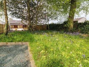 A garden with a variety of flowers, a wooden bench, and a house in the background. - Ty Taid (Gaerwen)