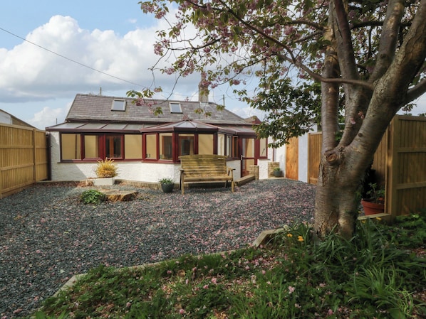 A house with a covered porch, a wooden bench, and a gravel driveway. - Ty Taid (Gaerwen)
