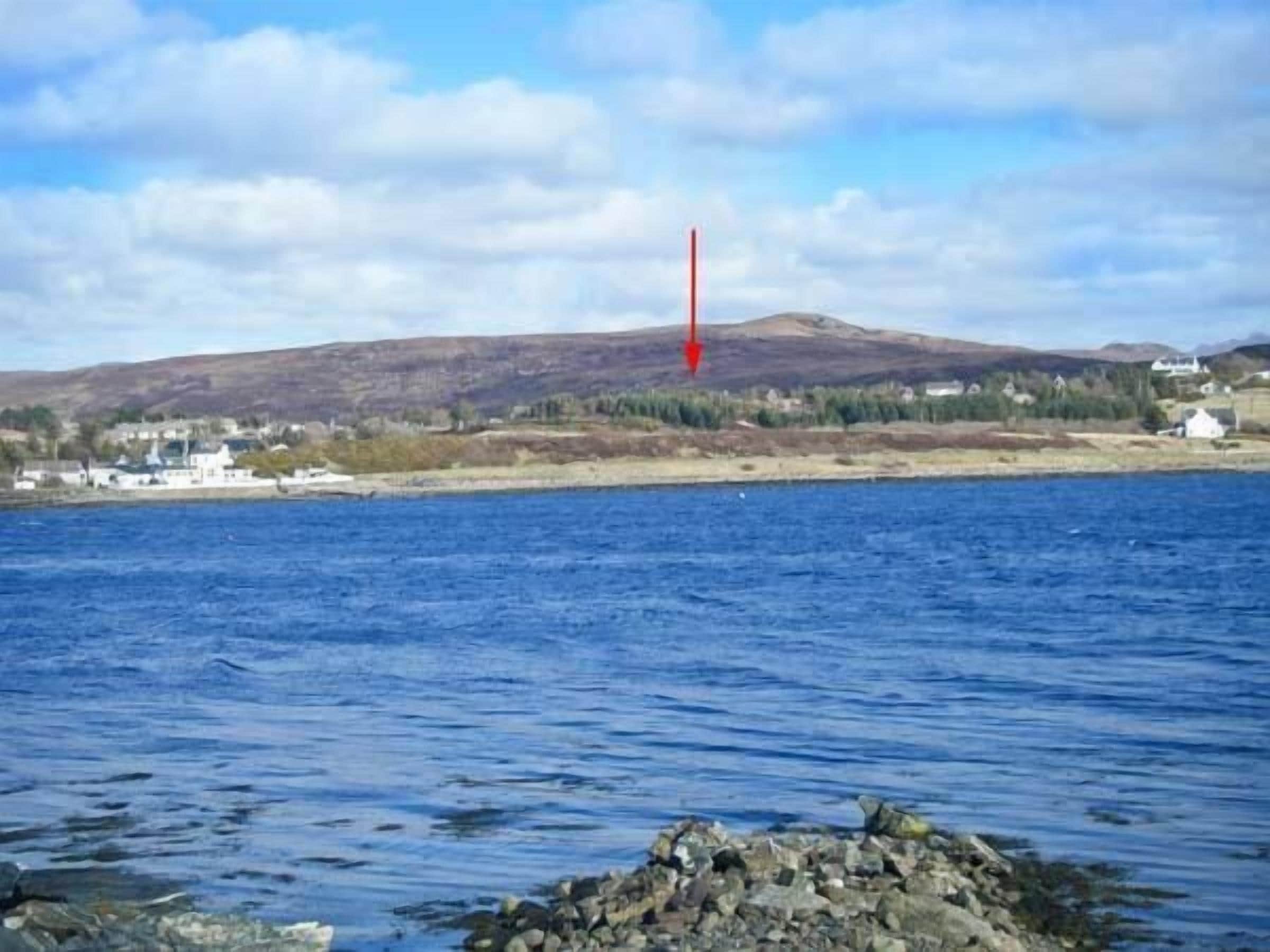 Un paysage côtier comprenant une étendue d’eau, une rive rocheuse et, au loin, une colline parsemée de bâtiments.