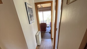 Un pasillo con un radiador, un cuadro en la pared y vistas a una habitación con una silla y un ventanal.