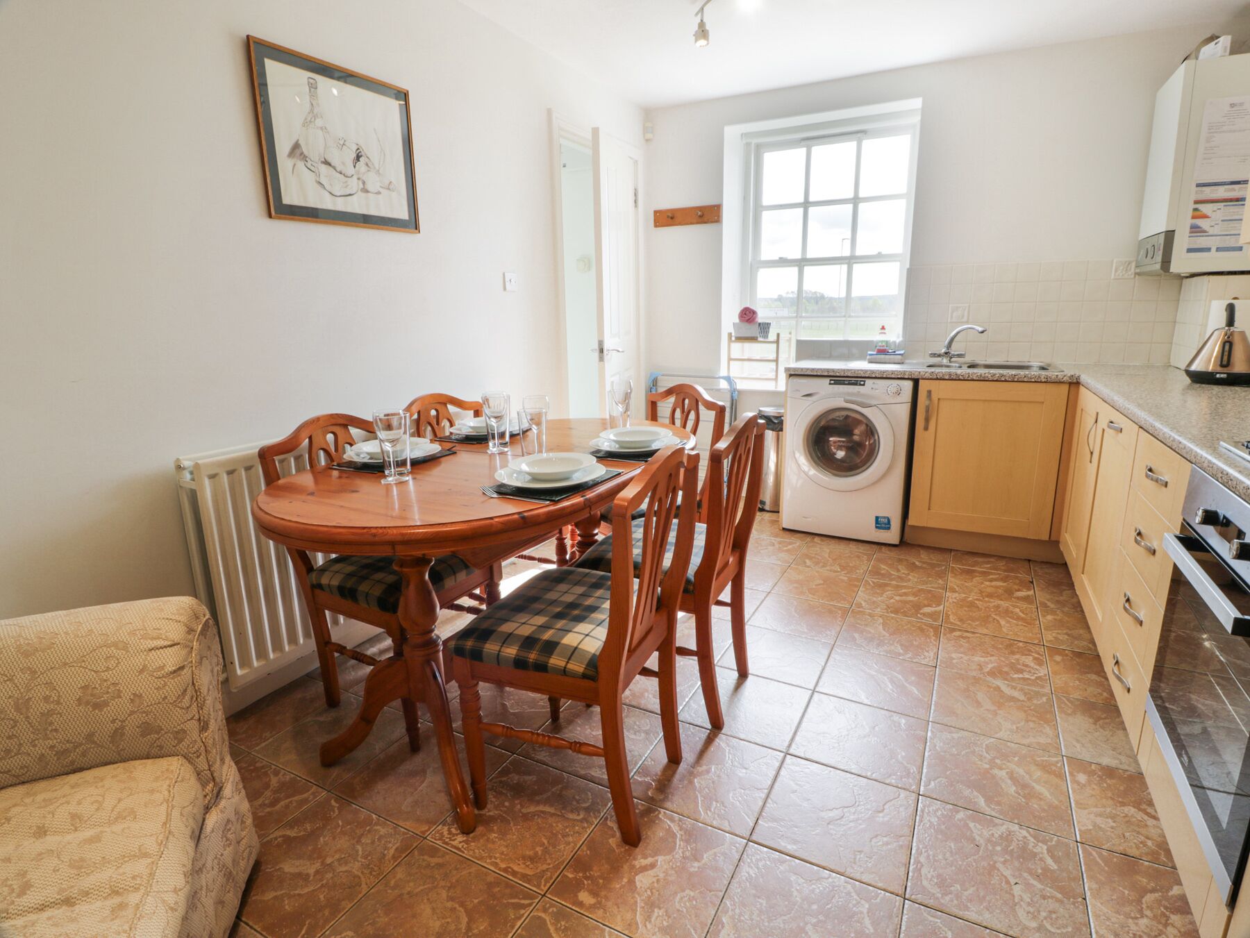 A dining area with a wooden table and chairs, a washing machine, and a kitchen with cabinets and a sink.