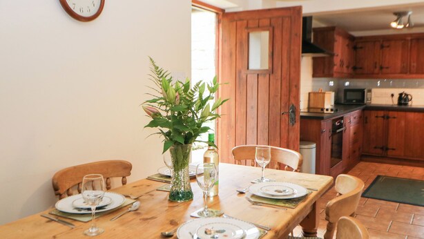 Une table à manger dressée pour quatre personnes, avec des assiettes, des couverts et des verres, un vase contenant des plantes vertes et une chaise en bois.