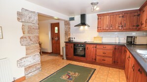 Une cuisine avec des meubles de rangement en bois, un four encastré, un four à micro-ondes et un mur en pierre.