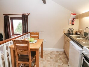 Cocina compacta con comedor, una ventana con cortinas, un lavamanos y una cafetera.