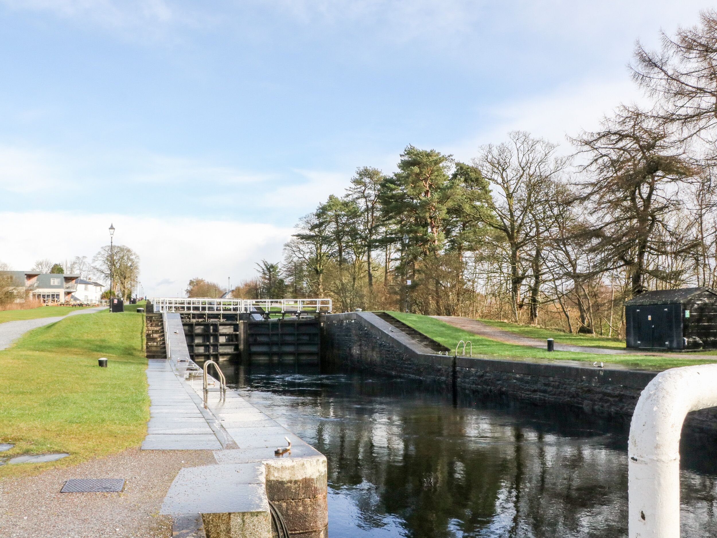 A lock gate on a canal with a grassy path and trees on either side.
