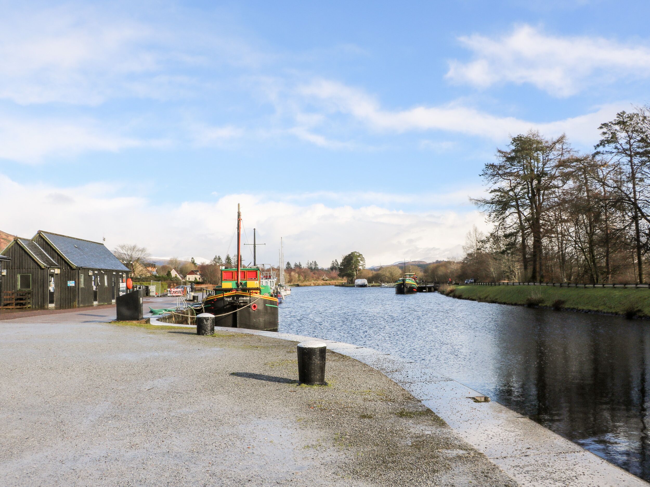 Een kade aan de rivier met een boot, een houten gebouw en een gazon.