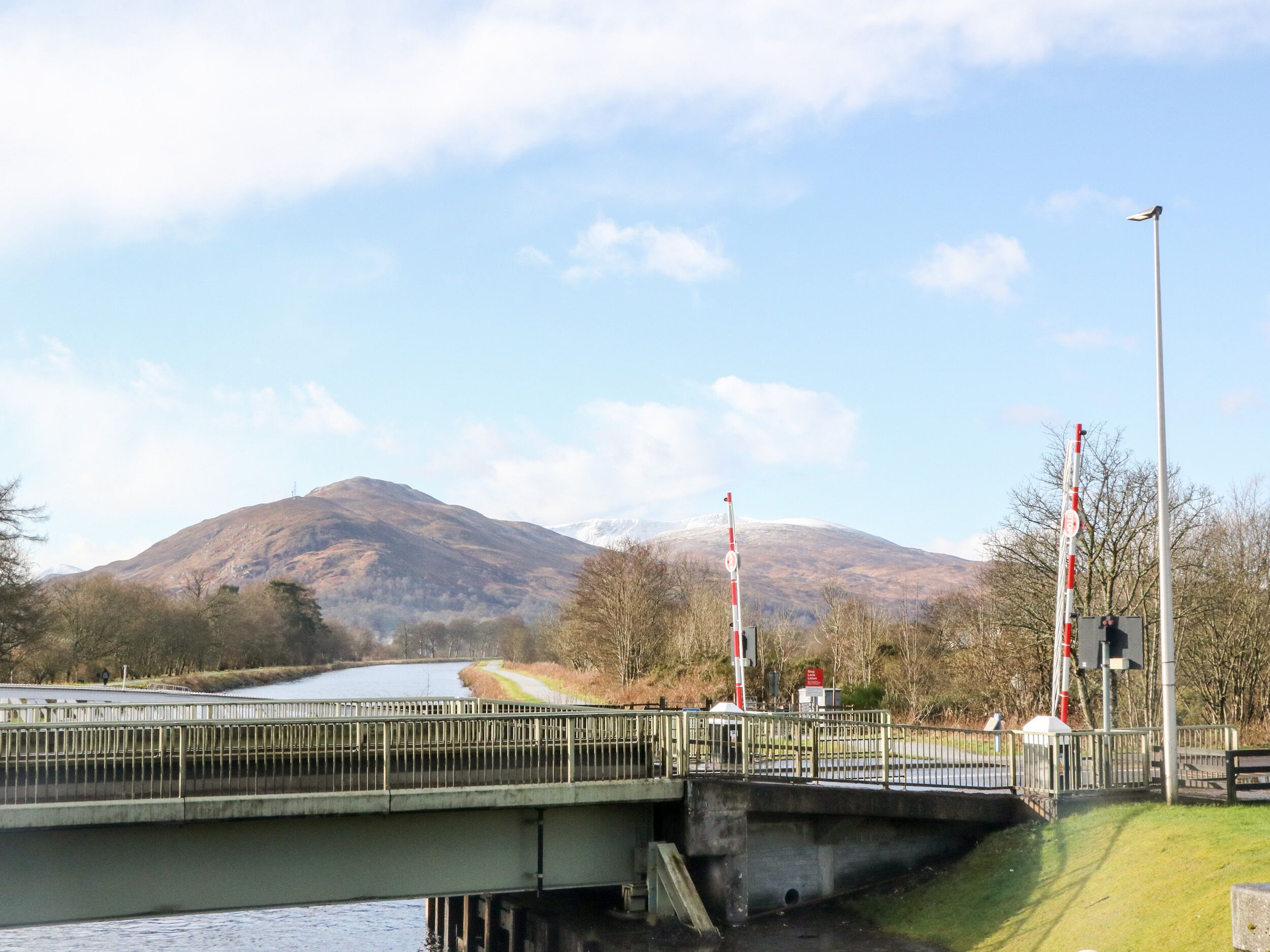 A bridge with a metal railing, a traffic signal, and a mountain in the background.