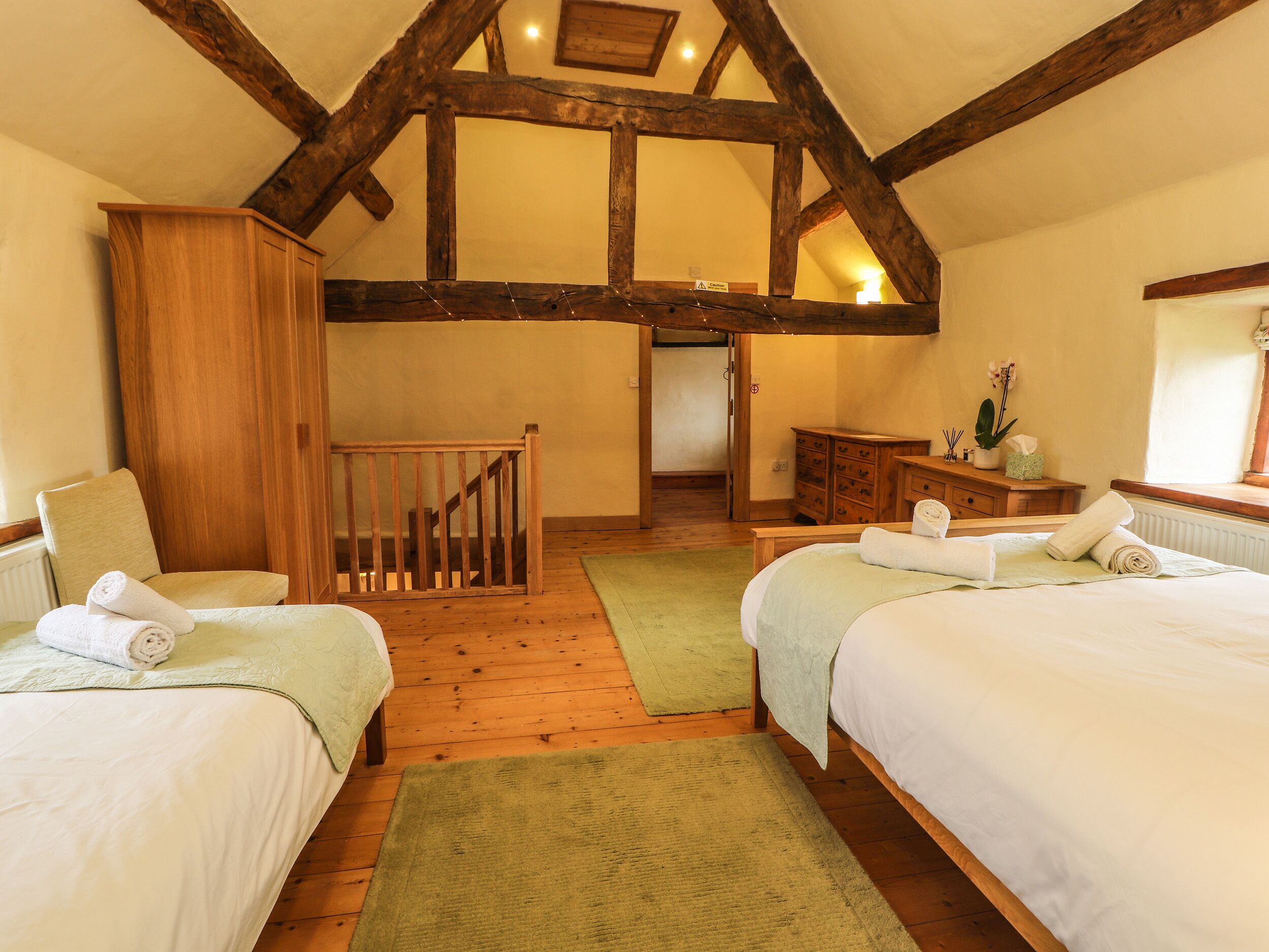 Een gezellige kamer met twee bedden, houten balken, een trap en een klein badgedeelte.