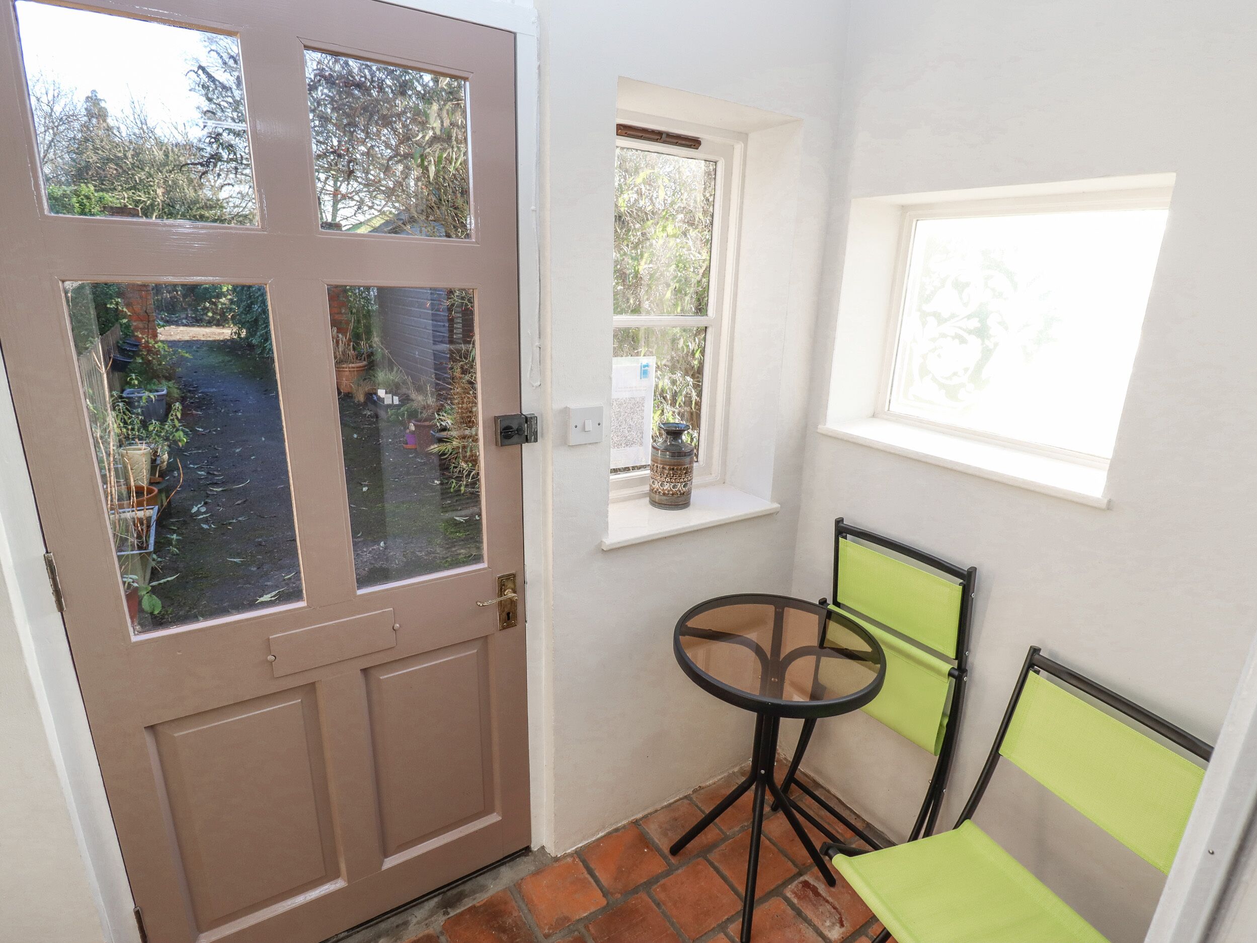 A small room with a brown door, a window, a small table, and a chair.