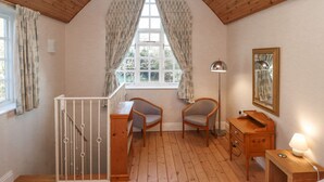 A cozy room with a wooden ceiling, a window with curtains, a desk with chairs, a lamp, and a mirror. - Ashfield Studio (Market Rasen)