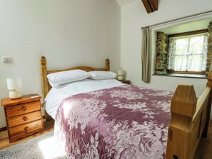 Une chambre à coucher avec un lit en bois, des oreillers blancs, une table de chevet en bois avec une lampe, et une fenêtre avec des rideaux.