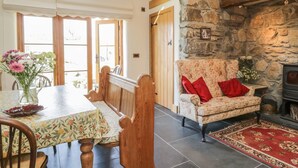 Une pièce chaleureuse avec une cheminée en pierre, un canapé à motifs floraux et un coin repas comprenant une table et des chaises.