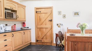 Une cuisine avec des armoires en bois, un four à micro-ondes et une porte en bois. Il y a des tableaux au mur et un vase avec des fleurs sur la table.