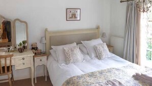 Une chambre à coucher avec un lit, des tables de chevet, un miroir et une fenêtre avec des rideaux.