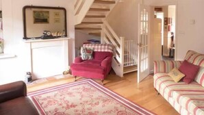 Un salon chaleureux avec un escalier en bois, un fauteuil rouge, un canapé à rayures et un tapis à motifs floraux.