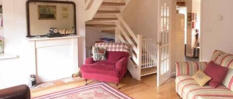 A cozy living room with a wooden staircase, a red armchair, a striped sofa, and a floral rug.