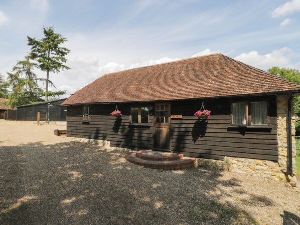 A wooden building with a tiled roof, a gravel driveway, and hanging flower baskets. - Bolton Barn (Maidstone)