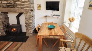 Una habitación acogedora con chimenea de piedra, una mesa de comedor de madera y un televisor montado en la pared.