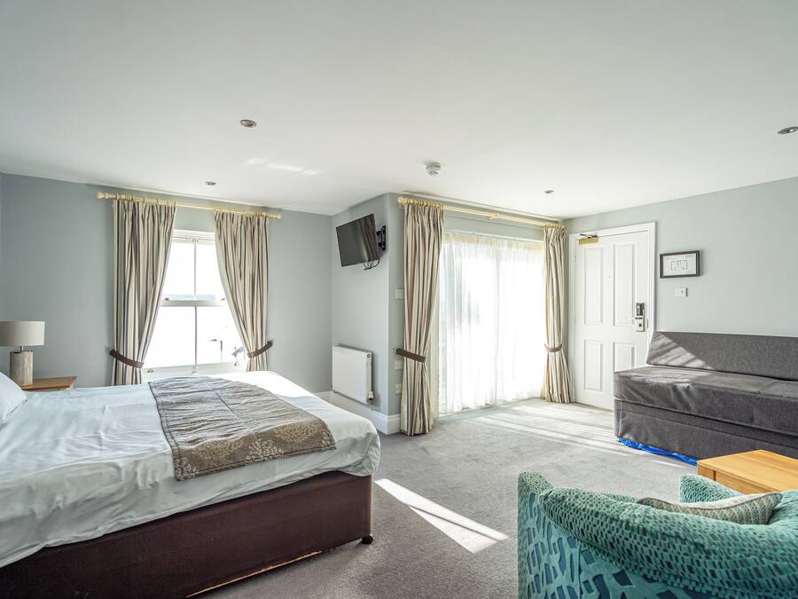 A hotel room with a large bed, a sofa, a TV mounted on the wall, and a window with curtains.