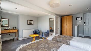 A hotel room with two beds, a wooden desk, a small round table, and a wardrobe.