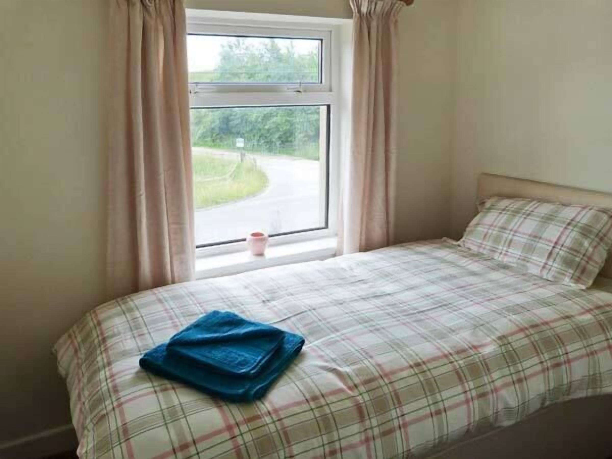 A bedroom with a bed, a window with curtains, and a view of a road and greenery outside.