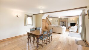 A spacious living area with a wooden dining table, a sofa set, and a stone fireplace. - Groves Fishleigh (Okehampton)