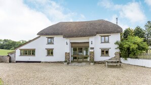 A two-story house with a thatched roof, stone walls, and a gravel driveway. - Groves Fishleigh (Okehampton)