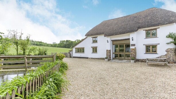 A white house with a thatched roof, a gravel driveway, and a wooden fence. - Groves Fishleigh (Okehampton)