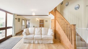 A spacious living room with a wooden staircase, a white leather sofa, and a bookshelf. - Groves Fishleigh (Okehampton)