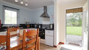 A modern kitchen with a dining area, a stainless steel range hood, and a view of the outdoors through a sliding glass door.