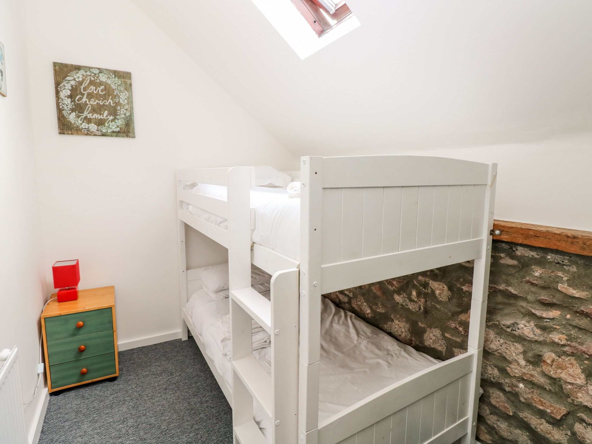A bunk bed room with a small wooden nightstand and a framed sign on the wall.