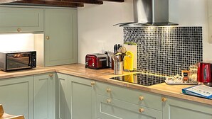 Una cocina con armarios verde claro, encimera de madera, microondas, tostadora y hervidor.