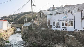A riverside building with a sign for 'SBLASH CABAN PYSGOD-FISH BAR' and a stone wall.