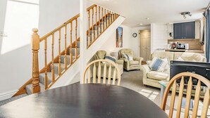 A living room with a staircase, a dining table, and a kitchen area. - West Sea View No 5 (Yarmouth)