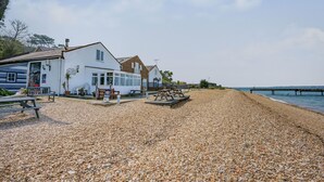 A coastal building with a pebbled beach in front, a pier extending into the water, and a clear sky. - West Sea View No 4 (Yarmouth)