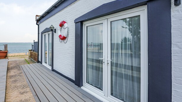 A coastal building with a deck, large sliding glass doors, and a lifebuoy on the wall. - West Sea View No 4 (Yarmouth)